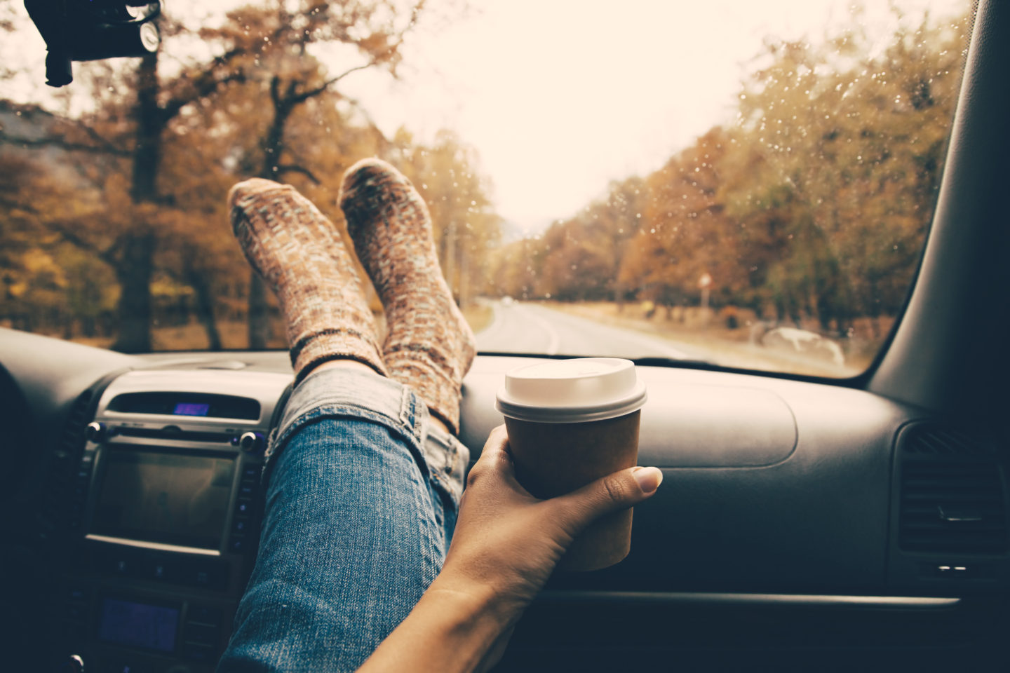 oman feet in warm socks on car dashboard with coffee in hand
